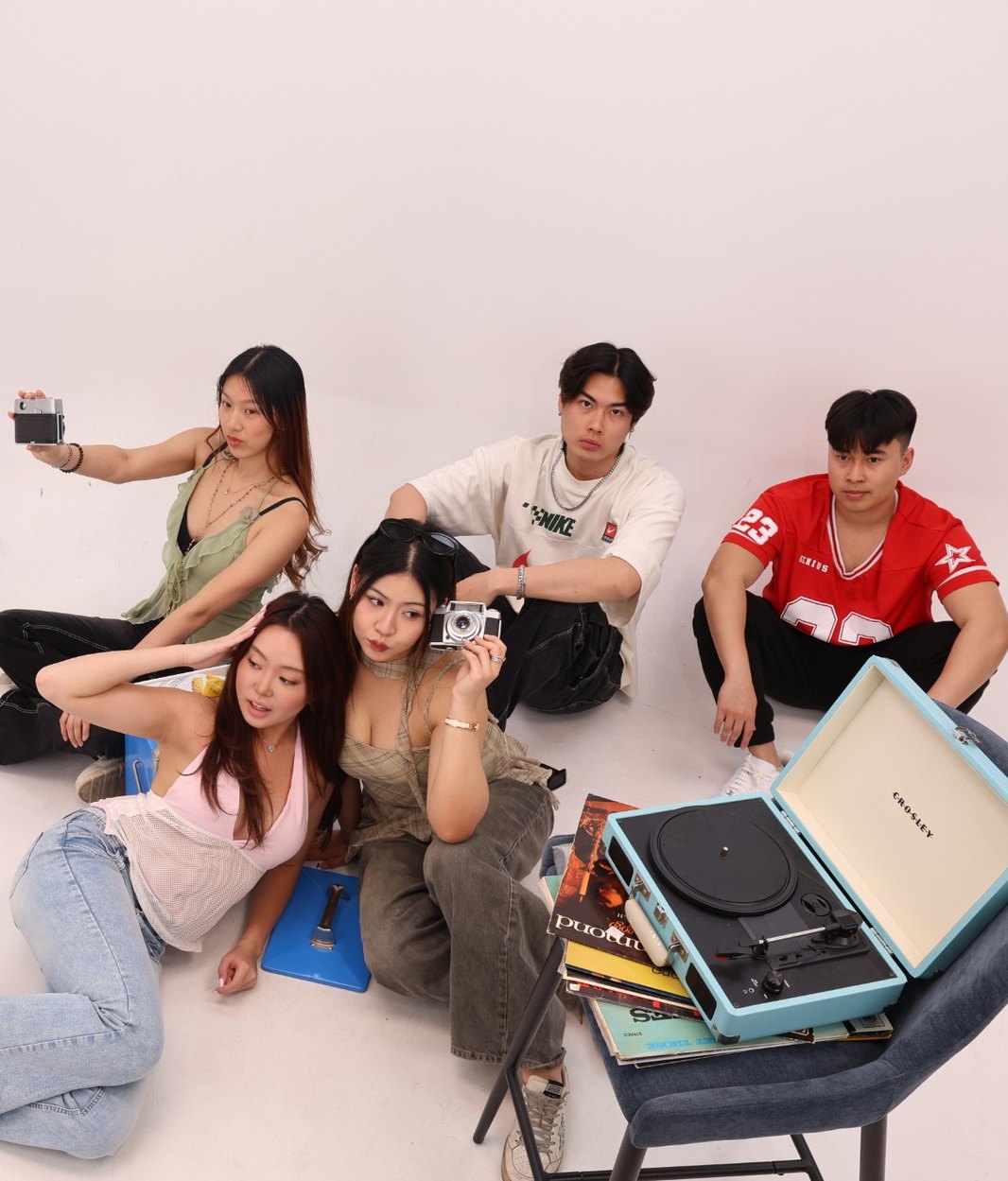 Five friends sitting on the studio floor with vintage cameras, vinyl records and a turntable