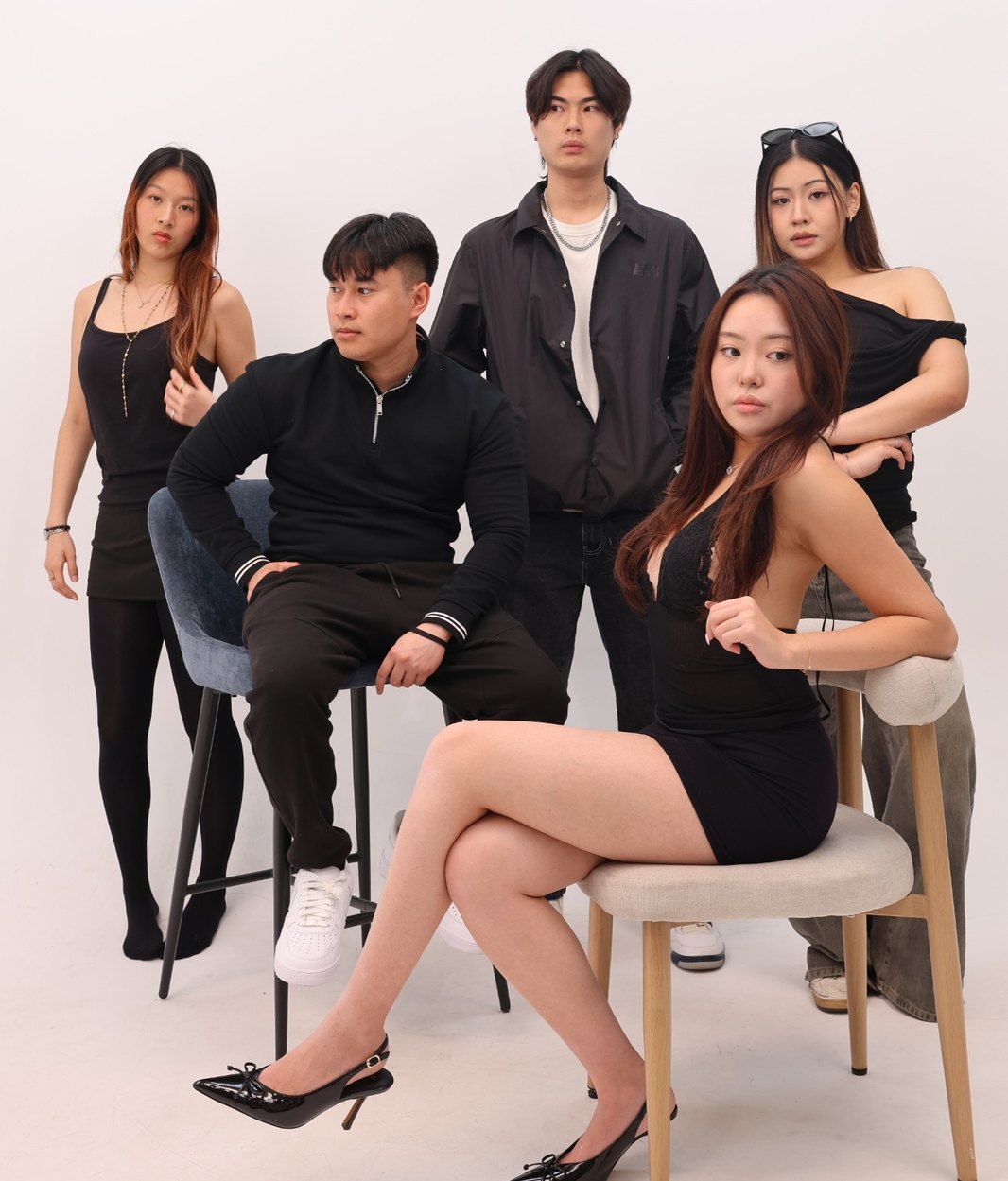 Five friends dressed in black posing together on stools against a white backdrop